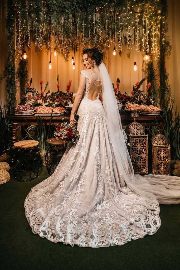 An elegant bride in a lace gown stands in a beautifully decorated indoor wedding setting.